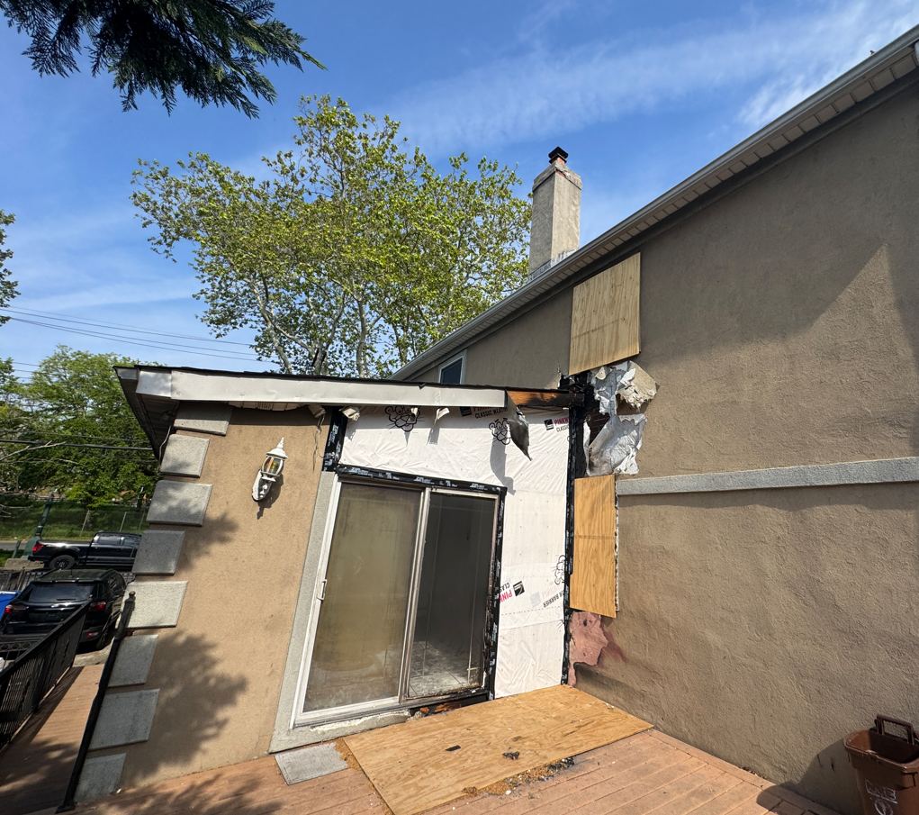 Fire-damaged rear exterior with charred framing exposed and openings boarded